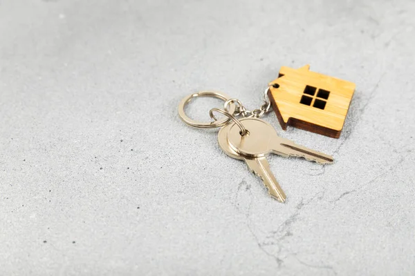 Keychain in the shape of a house with a key ring on a textured background. Concepts for real estate and moving home or renting property. Buying a property. Mock-up keychain house shaped.