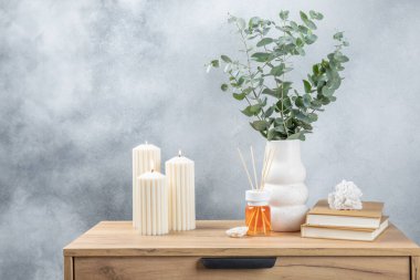 Yeşil okaliptüs, bir vazo tezgahında, çekmecelerden oluşan bir sandıkta duvarın arka planında durur. Aromaterapi. Çok güzel bir okaliptüs buketi. Çiçekler, mumlar ve aroma yayıcı ile minimalist iç mekan..