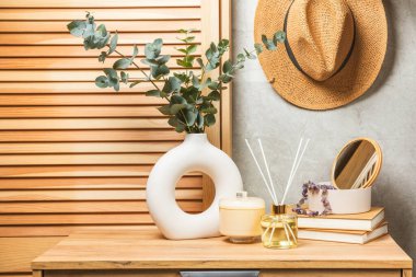 Yeşil okaliptüs, bir vazo tezgahında, çekmecelerden oluşan bir sandıkta duvarın arka planında durur. Aromaterapi. Çok güzel bir okaliptüs buketi. Çiçekler, mumlar ve aroma yayıcı ile minimalist iç mekan..