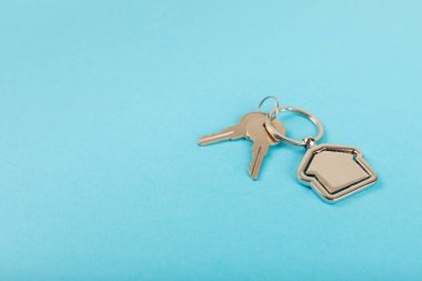 Arka planda anahtarlık olan ev şeklinde anahtarlık. Gayrimenkul ve eve taşınma ya da mülk kiralama kavramları. Mülk almak. Model anahtarlık evi şekillendirildi. Boşluğu kopyala.