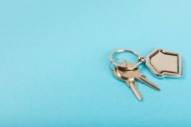 Arka planda anahtarlık olan ev şeklinde anahtarlık. Gayrimenkul ve eve taşınma ya da mülk kiralama kavramları. Mülk almak. Model anahtarlık evi şekillendirildi. Boşluğu kopyala.