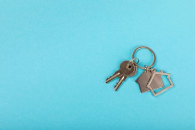 Arka planda anahtarlık olan ev şeklinde anahtarlık. Gayrimenkul ve eve taşınma ya da mülk kiralama kavramları. Mülk almak. Model anahtarlık evi şekillendirildi. Boşluğu kopyala.