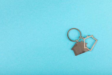 Arka planda anahtarlık olan ev şeklinde anahtarlık. Gayrimenkul ve eve taşınma ya da mülk kiralama kavramları. Mülk almak. Model anahtarlık evi şekillendirildi. Boşluğu kopyala.