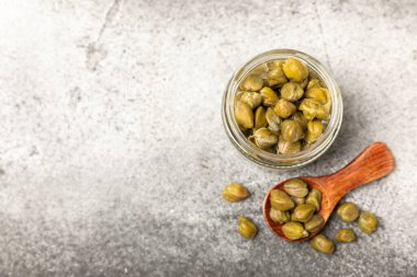 Ahşap mutfak masasında cam bir kavanozda kapari. Deniz tuzu ve biberiyeli kapari. Turşu turşusu. Akdeniz mutfağı malzemesi. Organik baharatlar ve baharatlar. Boşluğu kopyala.