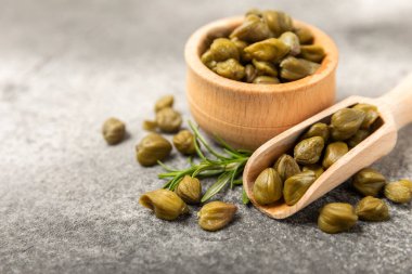 Ahşap mutfak masasında kapari. Deniz tuzu ve biberiyeli kapari. Turşu turşusu. Akdeniz mutfağı malzemesi. Organik baharatlar ve baharatlar. Boşluğu kopyala.