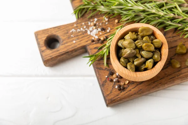 Ahşap mutfak masasında kapari. Deniz tuzu ve biberiyeli kapari. Turşu turşusu. Akdeniz mutfağı malzemesi. Organik baharatlar ve baharatlar. Boşluğu kopyala.