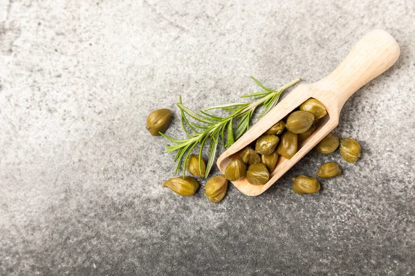 Ahşap mutfak masasında tahta bir kaşıkta kapari. Deniz tuzu ve biberiyeli kapari. Turşu turşusu. Akdeniz mutfağı malzemesi. Organik baharatlar ve baharatlar. Boşluğu kopyala.