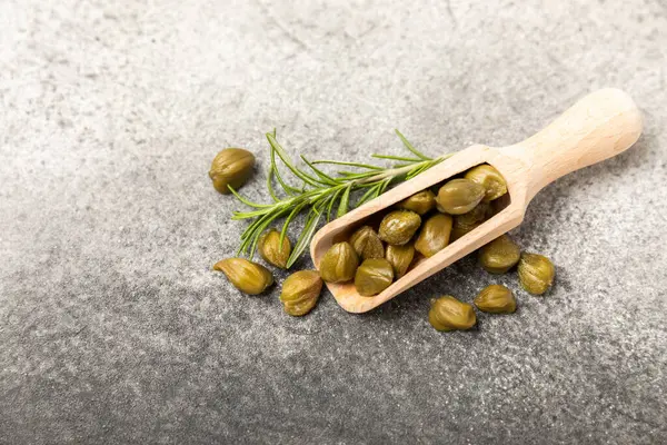 Ahşap mutfak masasında tahta bir kaşıkta kapari. Deniz tuzu ve biberiyeli kapari. Turşu turşusu. Akdeniz mutfağı malzemesi. Organik baharatlar ve baharatlar. Boşluğu kopyala.