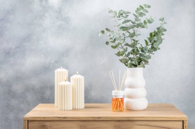 Yeşil okaliptüs, bir vazo tezgahında, çekmecelerden oluşan bir sandıkta duvarın arka planında durur. Aromaterapi. Çok güzel bir okaliptüs buketi. Çiçekler, mumlar ve aroma yayıcı ile minimalist iç mekan..