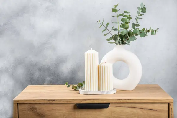 Green eucalyptus leaves in a vase stand on a chest of drawers against the background of a wall. Aromatherapy.Beautiful eucalyptus bouquet.Minimalist interior with flowers, candles and aroma diffuser.
