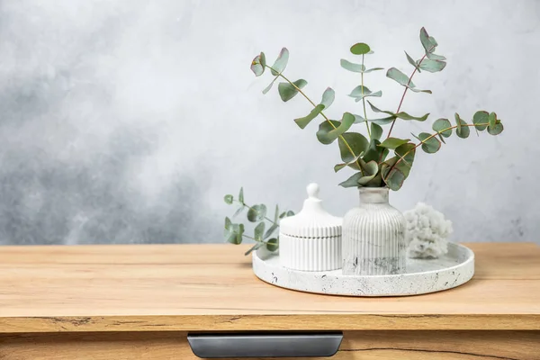 Green eucalyptus leaves in a vase stand on a chest of drawers against the background of a wall. Aromatherapy.Beautiful eucalyptus bouquet.Minimalist interior with flowers, candles and aroma diffuser.