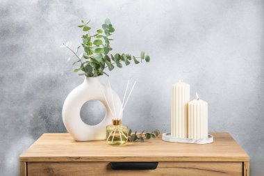 Yeşil okaliptüs, bir vazo tezgahında, çekmecelerden oluşan bir sandıkta duvarın arka planında durur. Aromaterapi. Çok güzel bir okaliptüs buketi. Çiçekler, mumlar ve aroma yayıcı ile minimalist iç mekan..