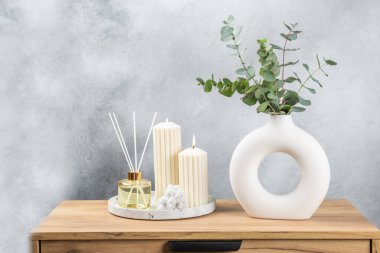 Yeşil okaliptüs, bir vazo tezgahında, çekmecelerden oluşan bir sandıkta duvarın arka planında durur. Aromaterapi. Çok güzel bir okaliptüs buketi. Çiçekler, mumlar ve aroma yayıcı ile minimalist iç mekan..