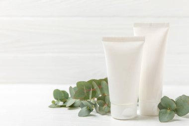 Beyaz ahşap zemin üzerinde okaliptüs yaprakları olan yüz, eller ve vücut için bir kavanoz nemlendirici kozmetik krem. Doğal organik ürün. Güzellik ve kaplıca konsepti. Vücut bakımı. Metin için boşluk. Boşluğu kopyala.