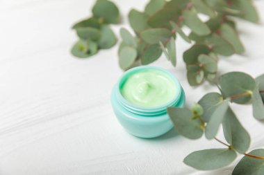 Beyaz ahşap zemin üzerinde okaliptüs yaprakları olan yüz, eller ve vücut için bir kavanoz nemlendirici kozmetik krem. Doğal organik ürün. Güzellik ve kaplıca konsepti. Vücut bakımı. Metin için boşluk. Boşluğu kopyala.