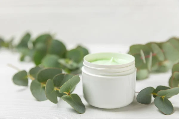 Jar of moisturizing cosmetic cream for face, hands and body with eucalyptus leaves on a white wooden background. Natural organic product. Beauty and spa concept. Body care. Space for text.Copy space.