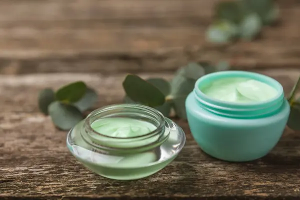 Jar of moisturizing cosmetic cream for face, hands and body with eucalyptus leaves on brown wooden background. Natural organic product. Beauty and spa concept. Body care. Space for text.Copy space.