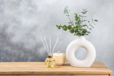 Yeşil okaliptüs, bir vazo tezgahında, çekmecelerden oluşan bir sandıkta duvarın arka planında durur. Aromaterapi. Çok güzel bir okaliptüs buketi. Çiçekler, mumlar ve aroma yayıcı ile minimalist iç mekan..