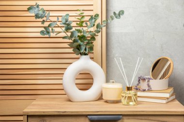 Yeşil okaliptüs, bir vazo tezgahında, çekmecelerden oluşan bir sandıkta duvarın arka planında durur. Aromaterapi. Çok güzel bir okaliptüs buketi. Çiçekler, mumlar ve aroma yayıcı ile minimalist iç mekan..