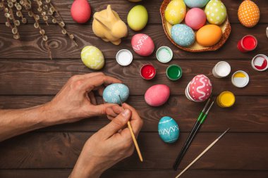 Erkek, paskalya yumurtalarını mutfak ahşap masasına boyar. Mutlu Paskalya kutlaması konsepti. Farklı şekillerde renkli paskalya yumurtaları..