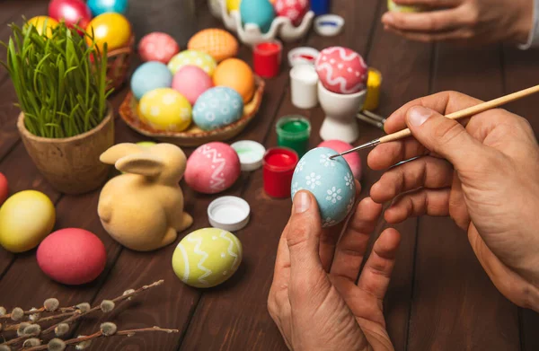 Man paints Easter eggs at the kitchen wooden table.Happy Easter celebration concept.Colorful Easter eggs with different patterns.Paints,decorations for coloring eggs for holiday.Creative background.