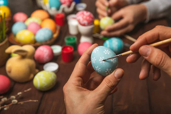 Man paints Easter eggs at the kitchen wooden table.Happy Easter celebration concept.Colorful Easter eggs with different patterns.Paints,decorations for coloring eggs for holiday.Creative background.