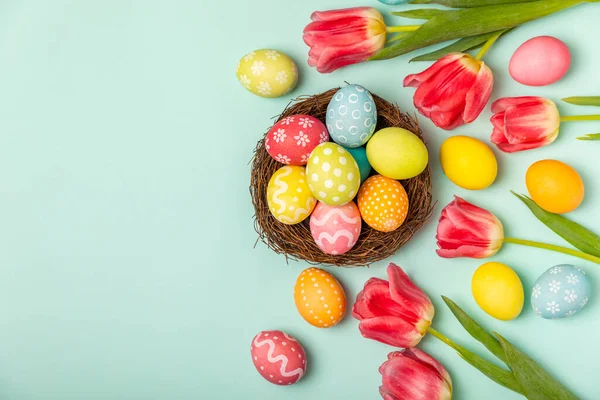 Paskalya yumurtaları ve parlak turkuaz arka planda bir buket lale. Paskalya kutlaması. El yapımı renkli Paskalya yumurtaları. Mesaj için yer. Boşluğu kopyala.
