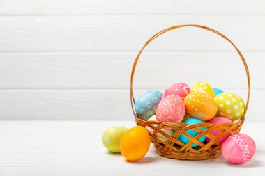 Renkli yumurtalarla dolu Paskalya sepeti ve ahşap bir masanın üzerinde bir buket lale. Paskalya kutlaması. El yapımı renkli Paskalya yumurtaları. Mesaj için yer. Boşluğu kopyala