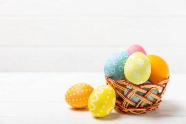 Renkli yumurtalarla dolu Paskalya sepeti ve ahşap bir masanın üzerinde bir buket lale. Paskalya kutlaması. El yapımı renkli Paskalya yumurtaları. Mesaj için yer. Boşluğu kopyala