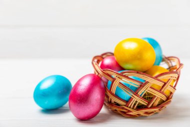 Renkli yumurtalarla dolu Paskalya sepeti ve ahşap bir masanın üzerinde bir buket lale. Paskalya kutlaması. El yapımı renkli Paskalya yumurtaları. Mesaj için yer. Boşluğu kopyala