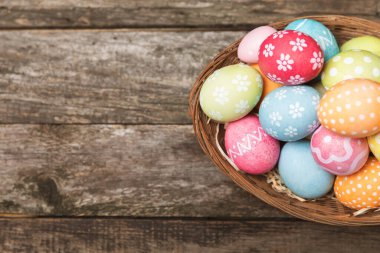Renkli yumurtalarla dolu Paskalya sepeti ve ahşap bir masanın üzerinde bir buket lale. Paskalya kutlaması. El yapımı renkli Paskalya yumurtaları. Mesaj için yer. Boşluğu kopyala
