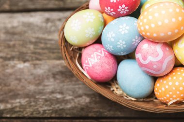 Renkli yumurtalarla dolu Paskalya sepeti ve ahşap bir masanın üzerinde bir buket lale. Paskalya kutlaması. El yapımı renkli Paskalya yumurtaları. Mesaj için yer. Boşluğu kopyala