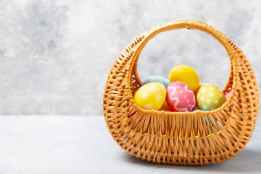 Renkli yumurtalarla dolu Paskalya sepeti ve ahşap bir masanın üzerinde bir buket lale. Paskalya kutlaması. El yapımı renkli Paskalya yumurtaları. Mesaj için yer. Boşluğu kopyala