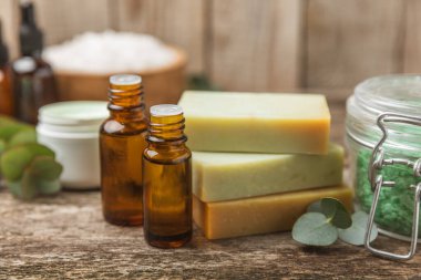 Tahta arka planda okaliptüs yapraklı güzel bir spa kompozisyonu. Vücut kremi, fırça, maske, temel yağ ve deniz tuzu içeren güzellik ve moda spa konsepti. Kozmetik ürün. Boşluğu kopyala.