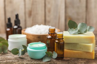 Tahta arka planda okaliptüs yapraklı güzel bir spa kompozisyonu. Vücut kremi, fırça, maske, temel yağ ve deniz tuzu içeren güzellik ve moda spa konsepti. Kozmetik ürün. Boşluğu kopyala.