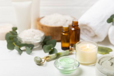 Tahta arka planda okaliptüs yapraklı güzel bir spa kompozisyonu. Vücut kremi, fırça, maske, temel yağ ve deniz tuzu içeren güzellik ve moda spa konsepti. Kozmetik ürün. Boşluğu kopyala.
