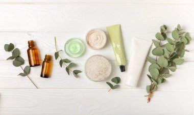 Tahta arka planda okaliptüs yapraklı güzel bir spa kompozisyonu. Vücut kremi, fırça, maske, temel yağ ve deniz tuzu içeren güzellik ve moda spa konsepti. Kozmetik ürün. Boşluğu kopyala.