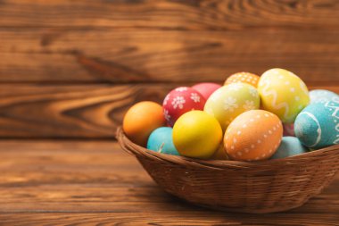 Renkli yumurtalarla dolu Paskalya sepeti ve ahşap bir masanın üzerinde bir buket lale. Paskalya kutlaması. El yapımı renkli Paskalya yumurtaları. Mesaj için yer. Boşluğu kopyala