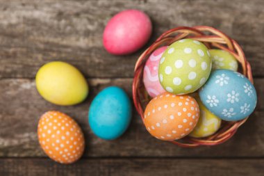 Renkli yumurtalarla dolu Paskalya sepeti ve ahşap bir masanın üzerinde bir buket lale. Paskalya kutlaması. El yapımı renkli Paskalya yumurtaları. Mesaj için yer. Boşluğu kopyala