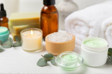 Tahta arka planda okaliptüs yapraklı güzel bir spa kompozisyonu. Vücut kremi, fırça, maske, temel yağ ve deniz tuzu içeren güzellik ve moda spa konsepti. Kozmetik ürün. Boşluğu kopyala.