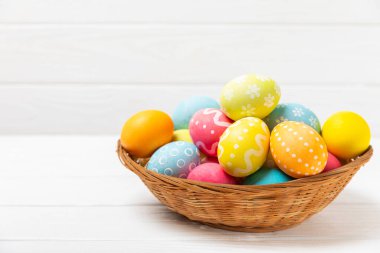 Renkli yumurtalarla dolu Paskalya sepeti ve ahşap bir masanın üzerinde bir buket lale. Paskalya kutlaması. El yapımı renkli Paskalya yumurtaları. Mesaj için yer. Boşluğu kopyala