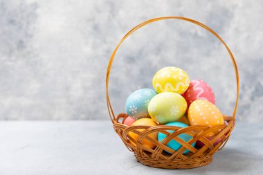 Renkli yumurtalarla dolu Paskalya sepeti ve ahşap bir masanın üzerinde bir buket lale. Paskalya kutlaması. El yapımı renkli Paskalya yumurtaları. Mesaj için yer. Boşluğu kopyala