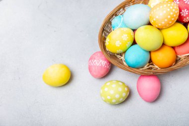 Renkli yumurtalarla dolu Paskalya sepeti ve ahşap bir masanın üzerinde bir buket lale. Paskalya kutlaması. El yapımı renkli Paskalya yumurtaları. Mesaj için yer. Boşluğu kopyala