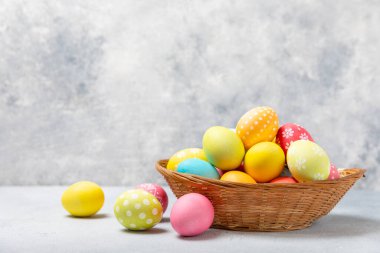 Renkli yumurtalarla dolu Paskalya sepeti ve ahşap bir masanın üzerinde bir buket lale. Paskalya kutlaması. El yapımı renkli Paskalya yumurtaları. Mesaj için yer. Boşluğu kopyala