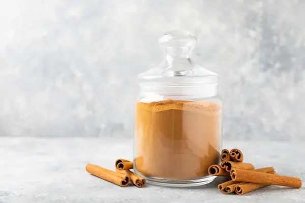 Cinnamon powder in a bowl on a textured wooden background. Spicy spice for baking, desserts and drinks. Fragrant ground cinnamon. Cinnamon stick. Place for text. Copy space.