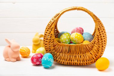 Renkli yumurtalarla dolu Paskalya sepeti ve ahşap bir masanın üzerinde bir buket lale. Paskalya kutlaması. El yapımı renkli Paskalya yumurtaları. Mesaj için yer. Boşluğu kopyala