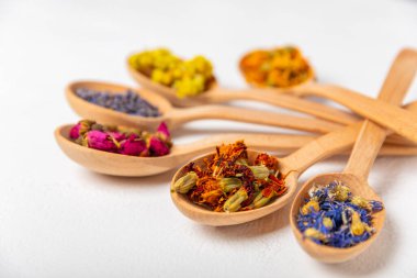 Ahşap bir zeminde ahşap kaşıklarda kurumuş bitki ve böğürtlen çayı. Şifalı şifalı bitkiler. Alternatif tıp konsepti. Linden, Calendula, Cornflowers, marigold, tansy, tea rose.