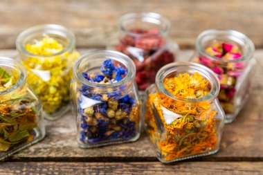 Ahşap bir arka planda cam kavanozlarda kurumuş bitki ve çilek çayı. Şifalı bitkiler. Alternatif tıp konsepti. Linden, Calendula, Cornflowers, marigold, tansy, tea rose.
