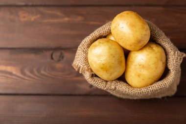 Genç patatesler Ahşap zeminde taze patates. Çuvalda patates. Hasat koleksiyonu. organik, taze kazılmış patatesler. Tarım geçmişi. Vejetaryen. Sebzeler. Mesajlar için yer. Boşluğu kopyala