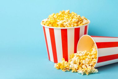 Patlamış mısır kutusu. Mavi arka planda kırmızı ve beyaz çizgili patlamış mısır kovaları. Sinema ve eğlence anlayışı. Patlamış mısırla film gecesi. Peynirli patlamış mısır. Lezzetli aperatif, aperatif. Metin için yer.